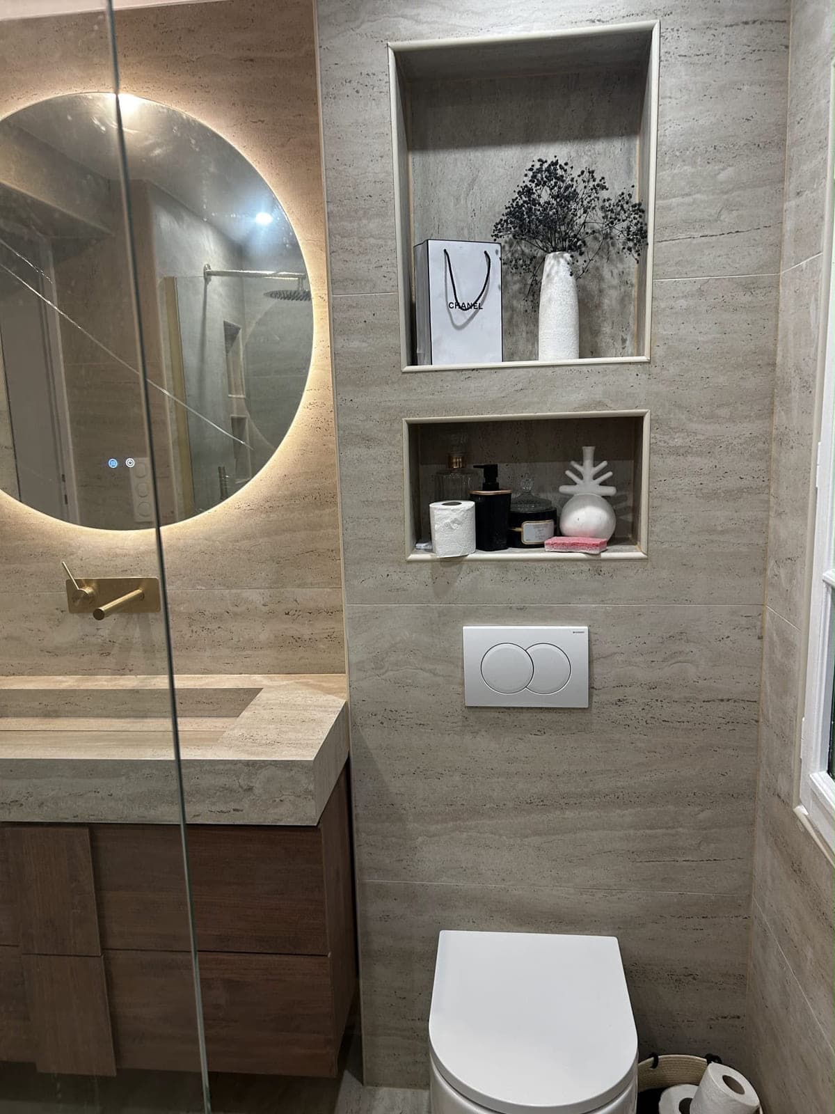 Niches de rangement maçonnées en travertin et miroir rond rétroéclairé