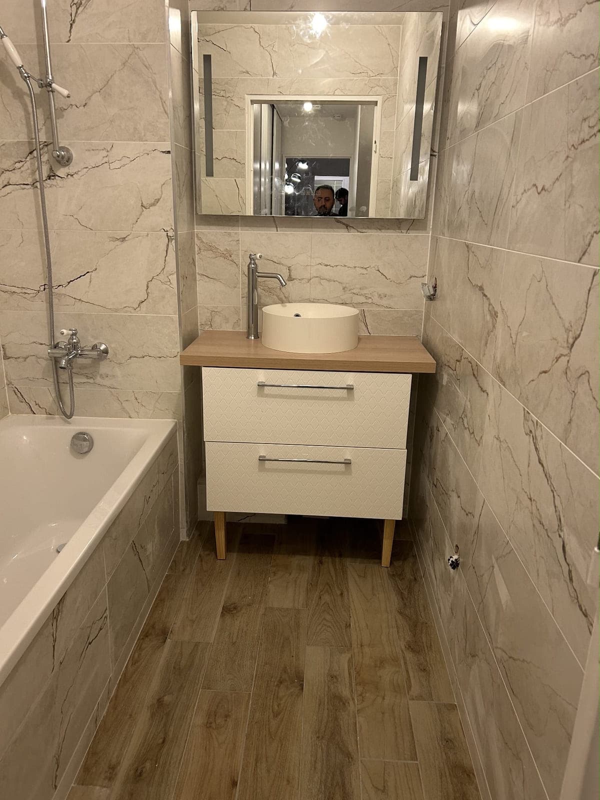 Vasque à poser sur plan bois dans une salle de bain carrelée façon marbre beige