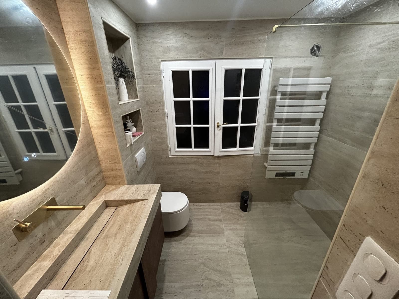 Salle de bain en travertin rénovée par HYDROBAT SOLUTIONS, douche de plain-pied et plan vasque sur mesure