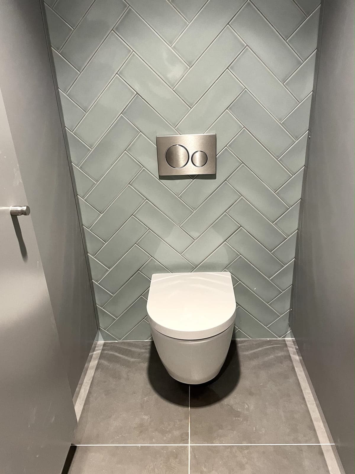 WC suspendu devant une faïence vert d'eau posée en chevrons